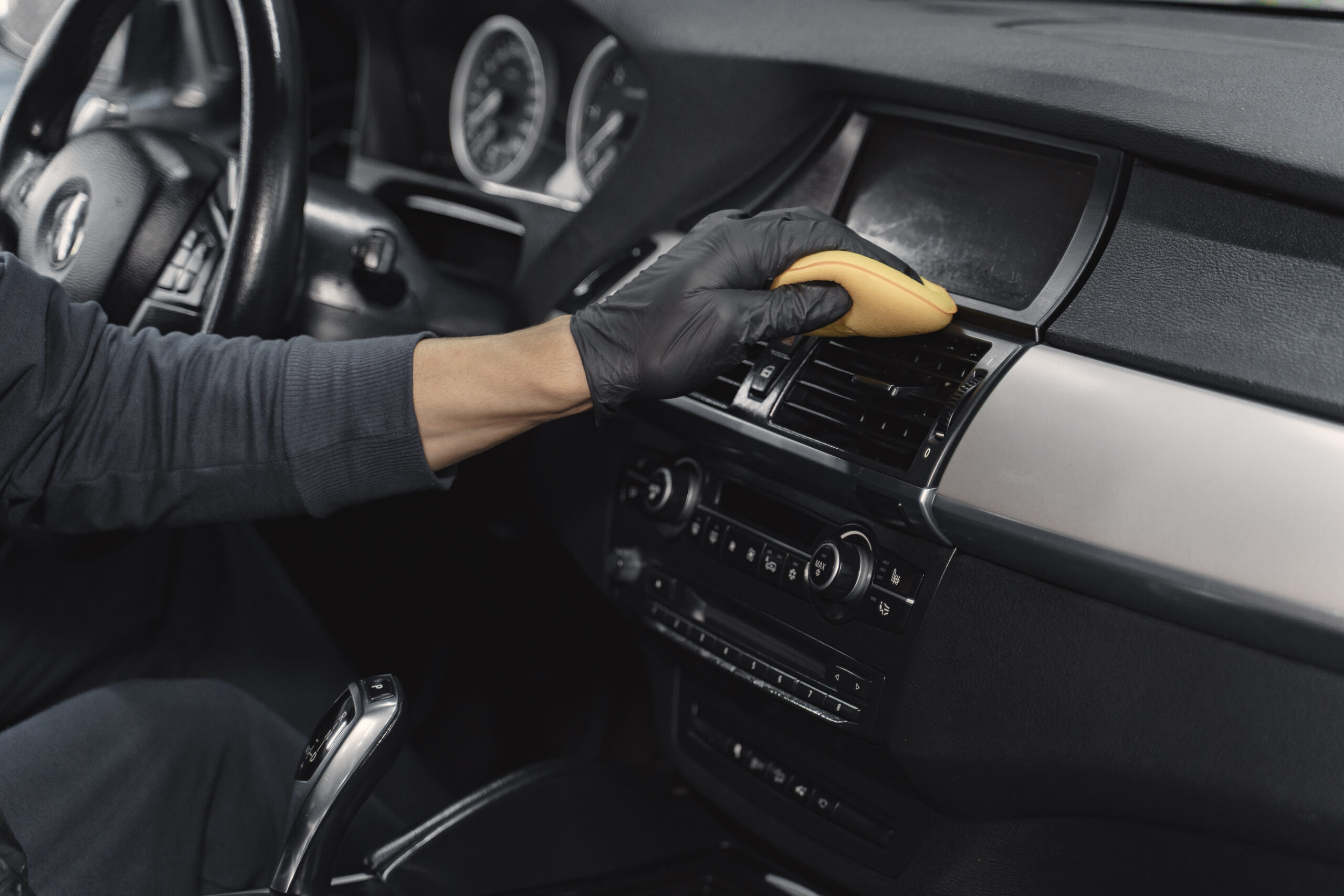 Man in a garage. Worker polish inside a car. Man in a black uniform.